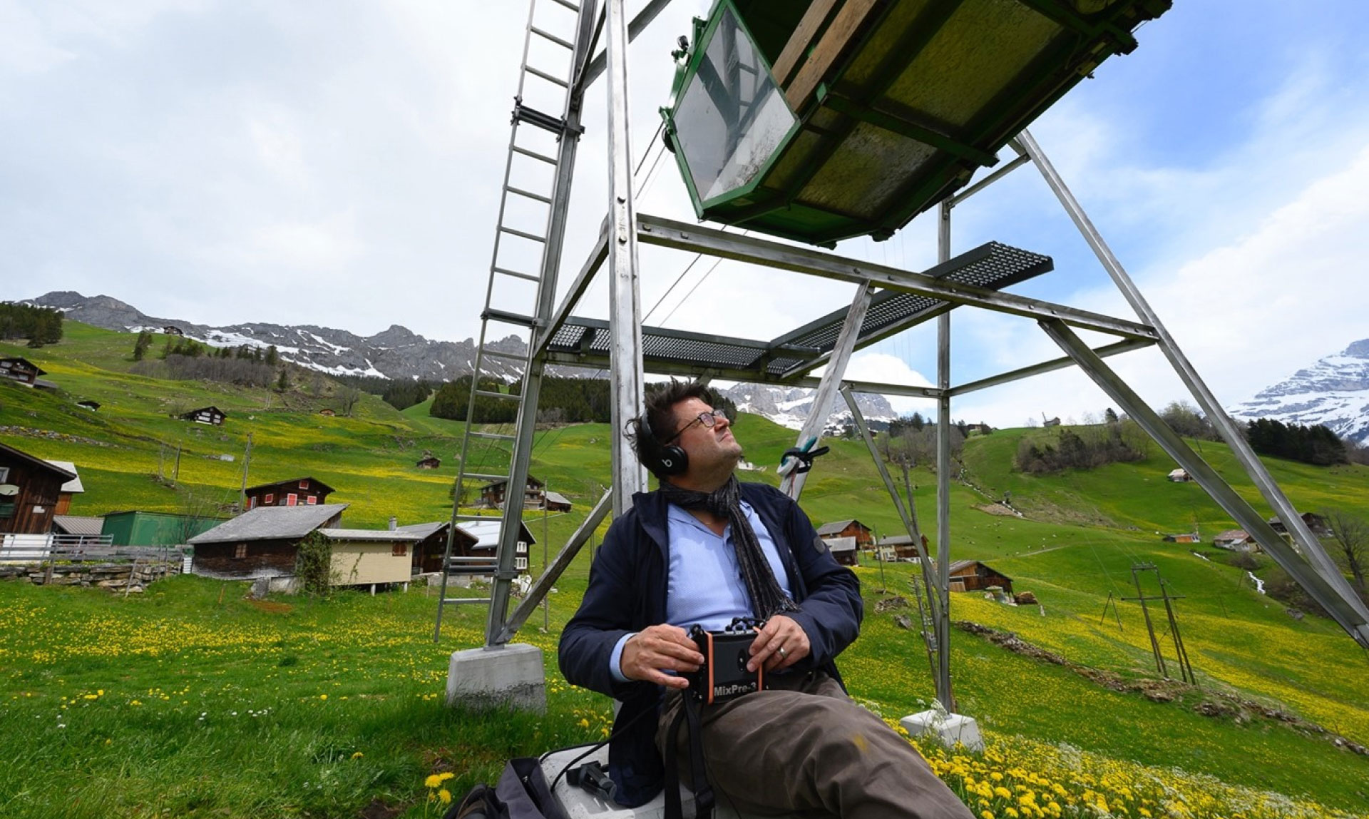 Person sitting underneath a Swiss alpine ropeway with a recording device